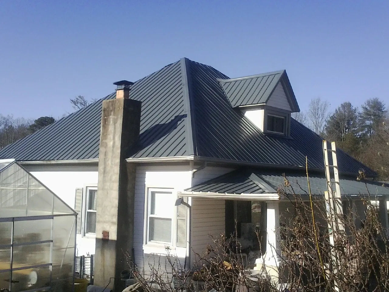 Dark blue standing seam metal roof on a white farmhouse with dormer — Slate & Tile Roof Repair by Roofing Brothers in Hollow Rock