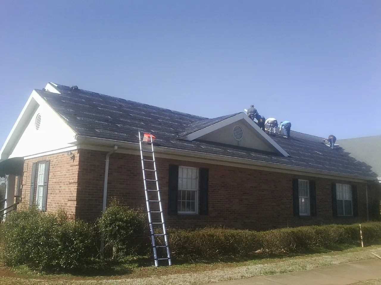 Crew tearing shingles off a brick ranch roof with a ladder set — Metal Roof Repair work by our crew in Hollow Rock