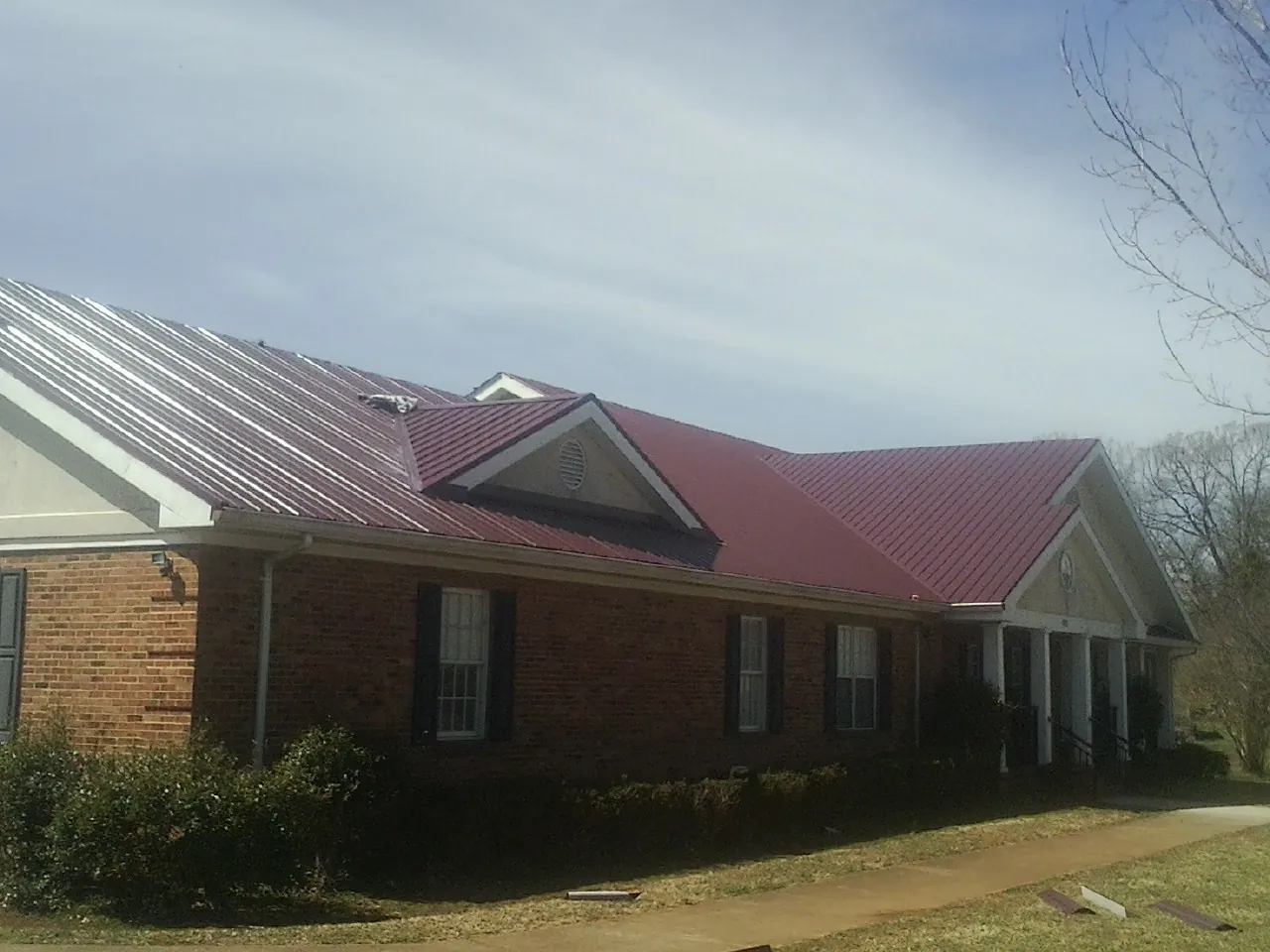 Red metal roof with gabled entries on a long brick building, from a Hail Damage Roof Repair job in Hollow Rock
