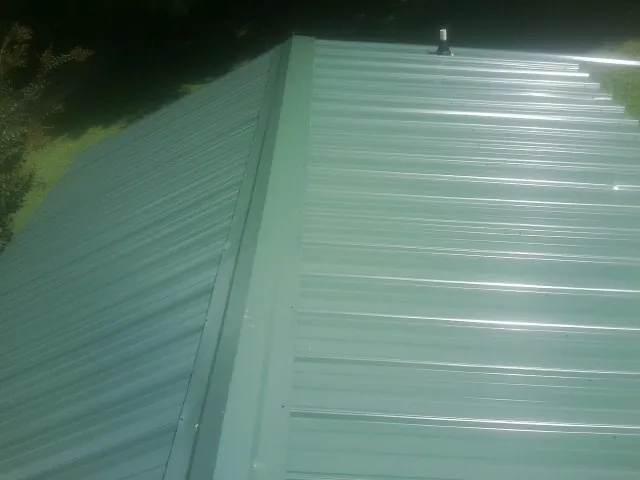 New green metal panels meeting at the ridge of a roof — Flat Roof Repair work by our crew in Hollow Rock