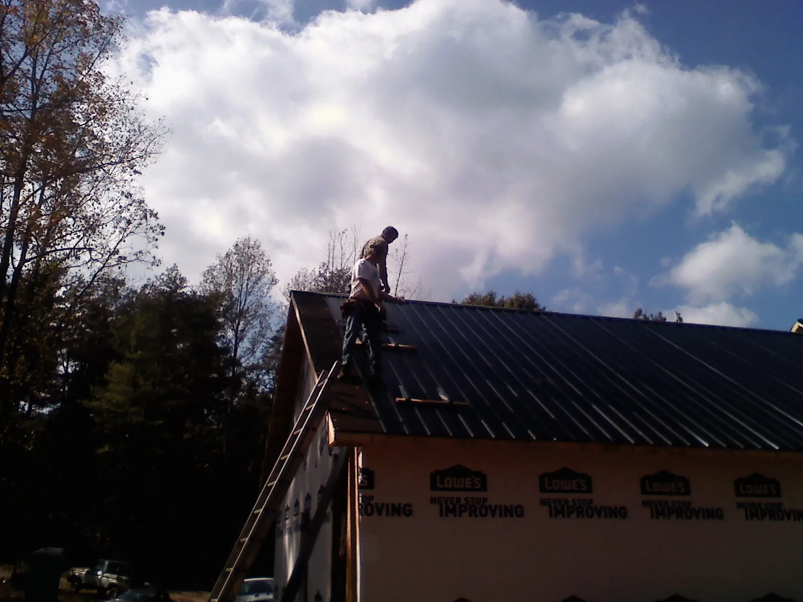 Roofer fastening dark metal panels high against a cloudy sky, from a Roof Inspection job in Hollow Rock