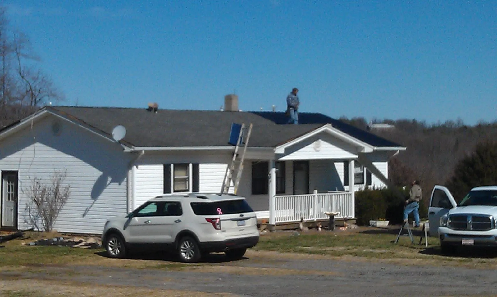 Roofers stripping shingles from a white ranch house roof in Hollow Rock