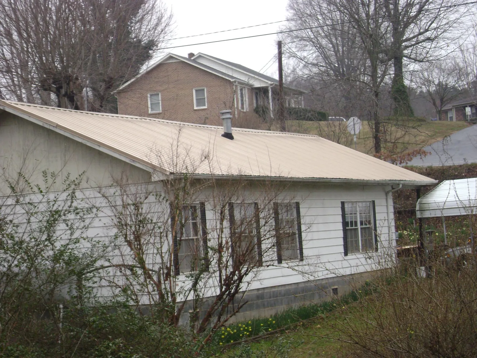 Tan metal roof on a white sided house set into a hillside — Commercial Roofing by Roofing Brothers in Hollow Rock