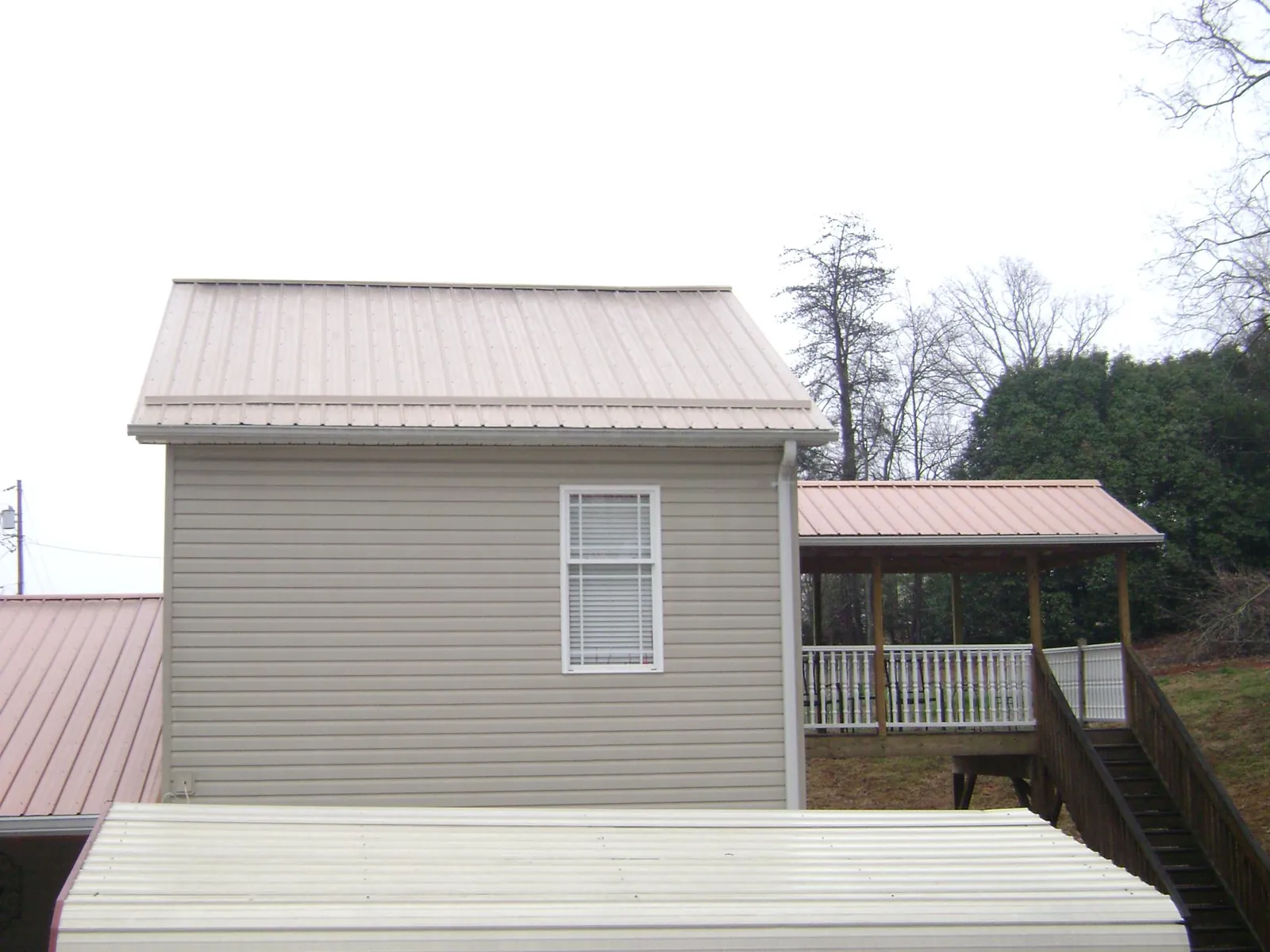 Tan metal roofs on a two story addition and attached porch, from a Roof Replacement job in Hollow Rock