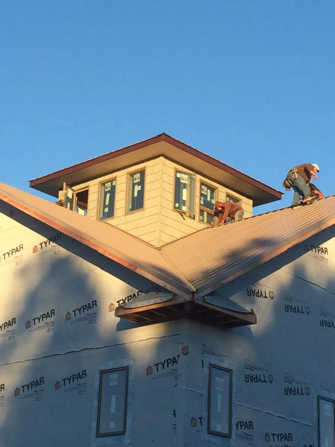 Roofers working around a rooftop cupola on a new metal roof at sunset — Roof Waterproofing in Hollow Rock by Roofing Brothers